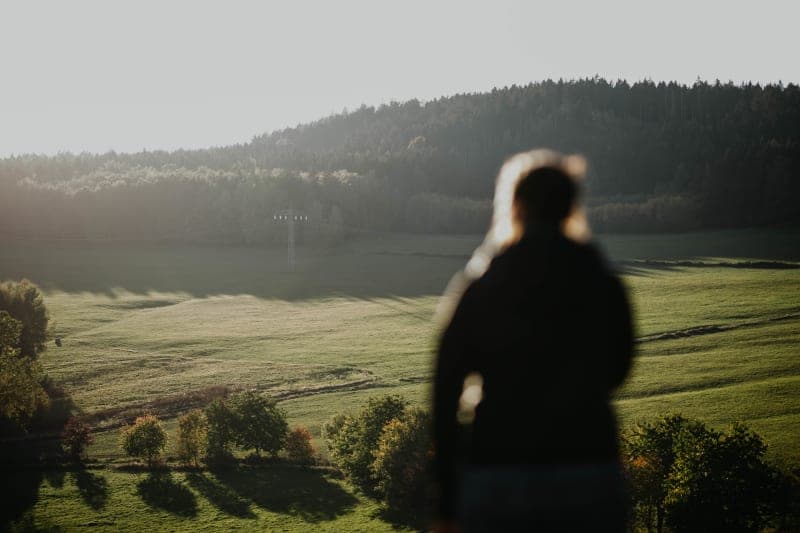 Person blickt auf nebelbedeckte Hügel und Wälder im goldenen Morgenlicht