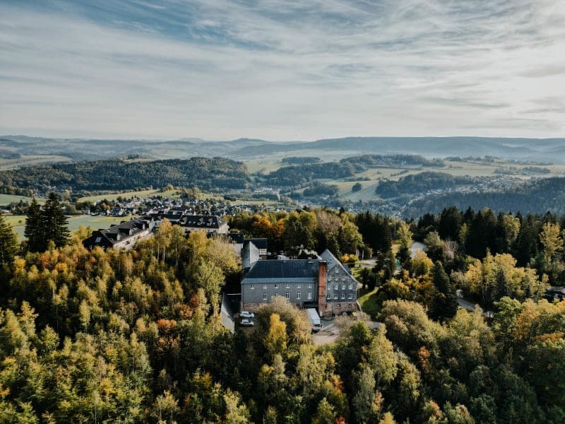 Luftaufnahme des Hotels Hoher Hahn umgeben von herbstlichem Mischwald im Erzgebirge