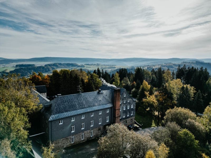 Luftaufnahme des Hotels Hoher Hahn umgeben von herbstlichem Wald und Morgennebel im Thüringer Wald
