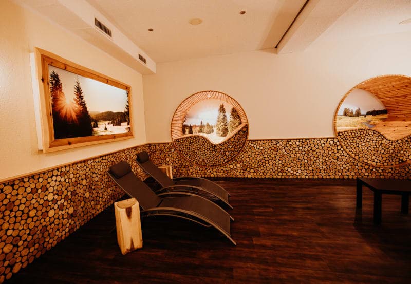 Ruheraum im Spa mit Holzscheiben-Wanddekoration, Relaxliegen und Blick auf Winterlandschaft