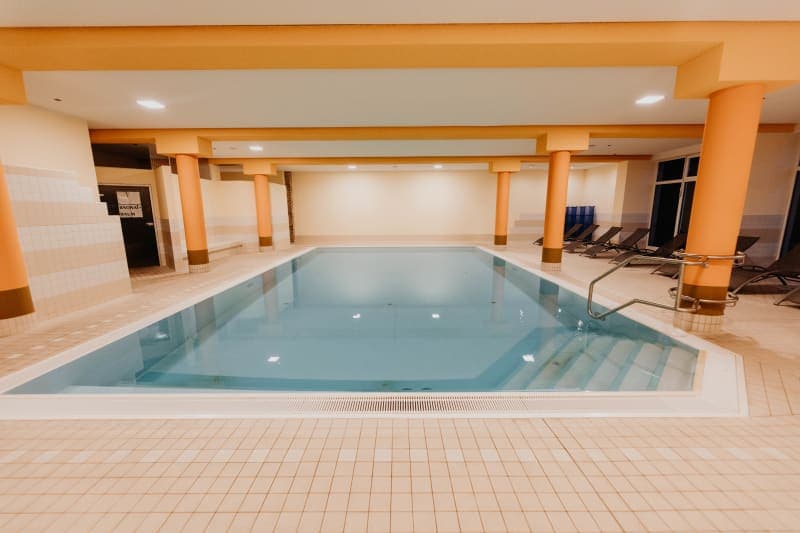 Innenpool mit Terrakotta-Säulen, klarem Wasser und Liegestühlen in warmem Ambiente