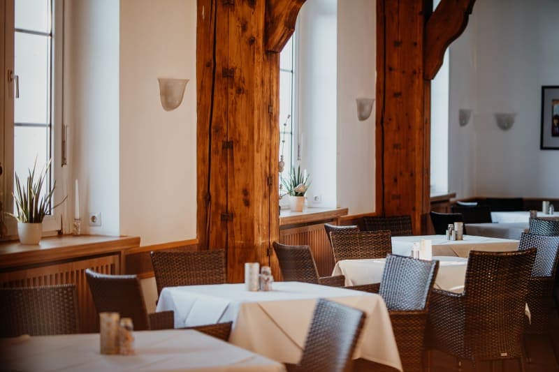 Veranstaltungsraum mit rustikalen Holzbalken, gedeckten Tischen und geflochtenen StĂĽhlen