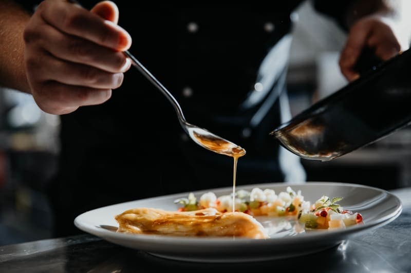 Koch richtet ein Gericht mit goldener Sauce im Restaurant Hoher Hahn an
